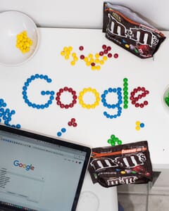 The word Google spelled out in M&Ms and Google homepage displayed on a laptop screen.